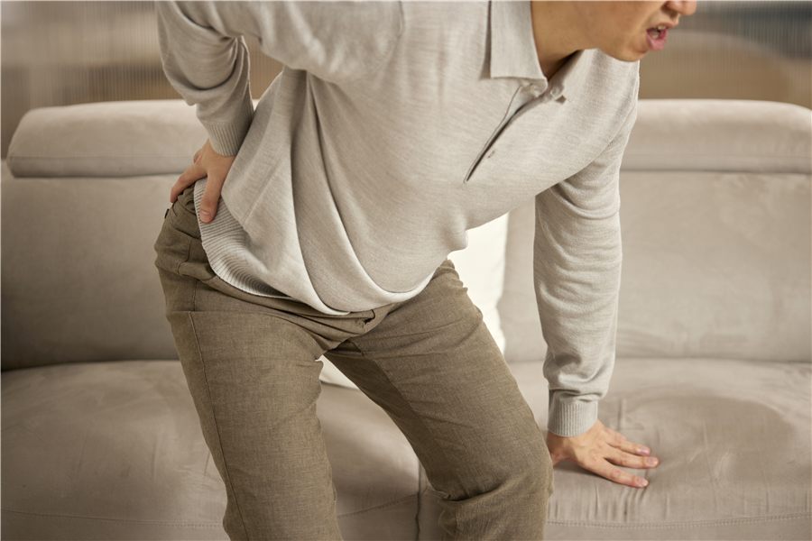 A person holding their lower back and struggling to get up from a sofa